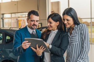 Shot of a handsome salesman showing documents to his happy clients at the dealership.