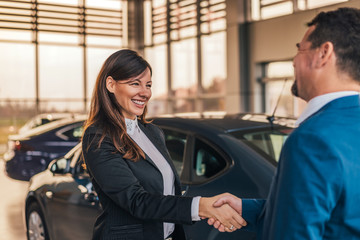 Cheerful car dealer handshake with customer in showroom. - obrazy, fototapety, plakaty