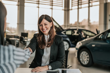 Saleswoman shaking hands with customer in car salon.