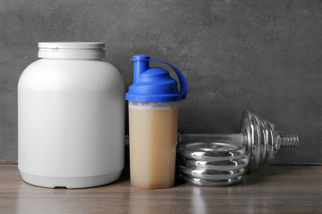 Composition with protein shake and dumbbell on table