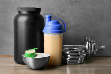 Composition with protein shake, powder and dumbbell on table