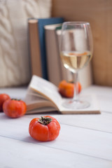Still life details, books, glass of wine and fruits on retro vintage wooden table in living room. Lazy winter weekend with a book, vertical, selective focus