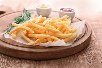 Wooden board with yummy french fries on table