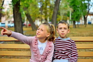 Brother and sister cuddling and sitting on a bench in a park on autumn day. Little girl and boy hugging