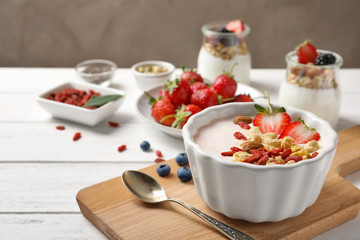 Tasty breakfast with goji berries in dish on wooden board