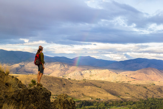 Woman stands on a cliff edge looking out at the mountainous scenery of the Methow Valley, WA