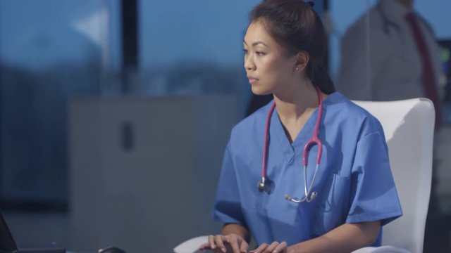  Nurse in modern hospital studying patient x rays & working on computer