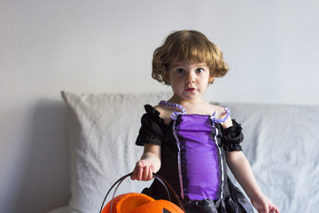 beautiful little girl standing on bed and wearing a halloween costume. playing with pumpkins. Home, indoors, lifestyle