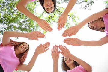 Young women in pink t-shirts joined in circle outdoors. Breast cancer awareness concept