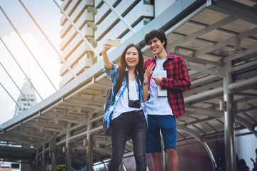 couple young beautiful asian woman and handsome caucasian man selfie by smartphone camera between traveling with modern building in big city, Bangkok Thailand travel concept.