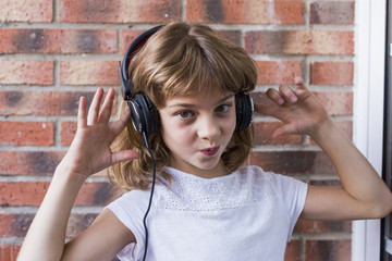 beautiful little girl with headphones at home listening to music and smiling, technology and music concept. Brick background. LIfestyle