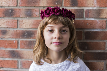 portrait of a beautiful little girl wearing a red crown roses on her head. Brick background. Lifestyle