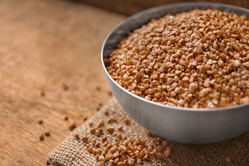 Metal bowl with raw buckwheat on table