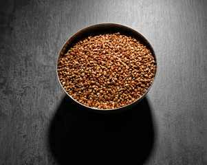 Bowl with raw buckwheat on dark background
