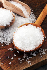 sea salt with wooden spoon and crystals of salt on wooden background.