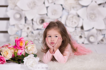 Obraz na płótnie Canvas Pretty girl with brunnete hair stylish dressed in pink dress pinky skirt shirt happyly smiling posing to camera for photosession in modern showroom studio on fur floor with paper flowers on wall.
