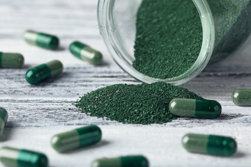Spirulina capsules with powder on table