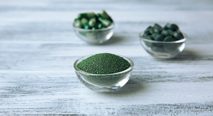 Bowls with spirulina powder, capsules and tablets on table