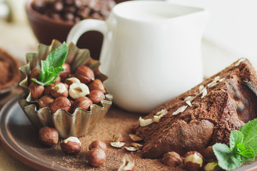 Piece of chocolate cake, mint leaves, hazelnuts and jar with milk