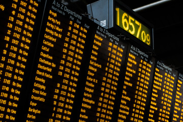 A train station destination board showing departure destinations and timings of trains at a large train station.