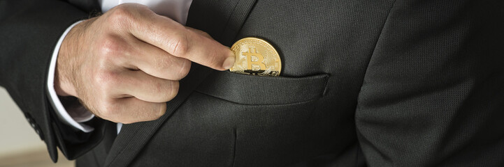 Businessman removing or placing  a golden bitcoin in a pocket