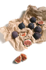 Whole and sliced in half figs in craft paper wrapping isolated on white background. Exotic food flat lay with copy space for text top view. Soft focus. Fresh and juicy 