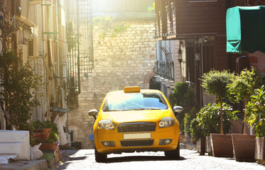 Taxi rides on a narrow street in the old town. Yellow taxicab on a sunny street.