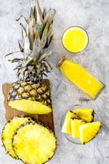 Non-alcoholic beverages. Bottle with fruit juice near pineapples slices on grey background top view