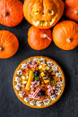Halloween tradition. Pumpkin pie and pumpkin with scary face on black background top view