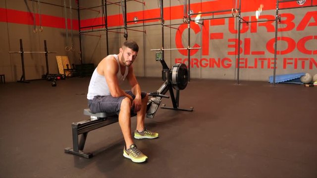 Male athlete sitting on rowing machine and looking at camera 