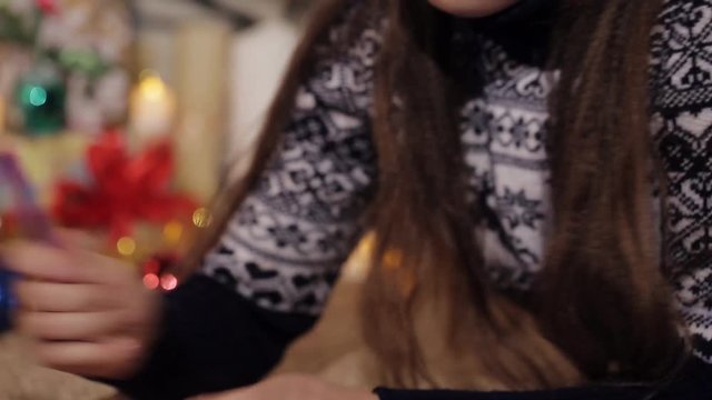 nice little girl with long hair on the background of Christmas gifts and lit candles wrote a letter to Santa Claus