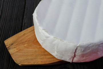 Round Camembert cheese on a wooden board.