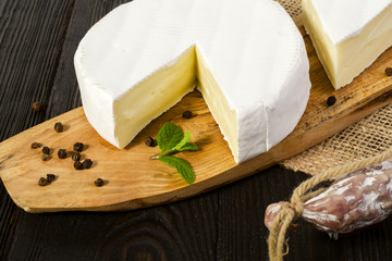 Round Camembert cheese, sliced, on a wooden board and fuet sausage, on a wooden board, with sack.
