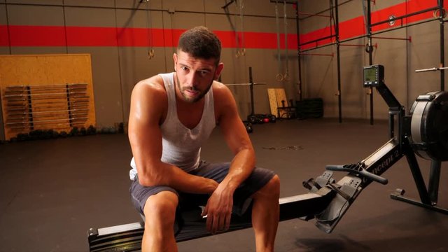 Male athlete sitting on rowing machine and looking at camera 