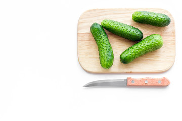 Make salad with fresh cucumbers. Vegetables on cutting board near knife on white background top view copyspace