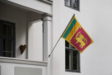 Sri Lanka flag displaying on a pole in front of the house. National flag of  Sri Lanka waving on a home hanging from a pole on a front door of a building.