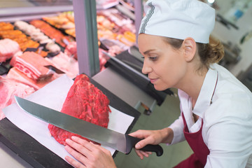 happy female butcher cutting meat at butchery counter
