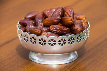 Dates fruit on a silver bowl on wooden table. The Muslim feast of the holy month of Ramadan Kareem