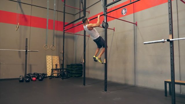Attractive male adult doing pull ups on bar and push ups in cross fit training gym