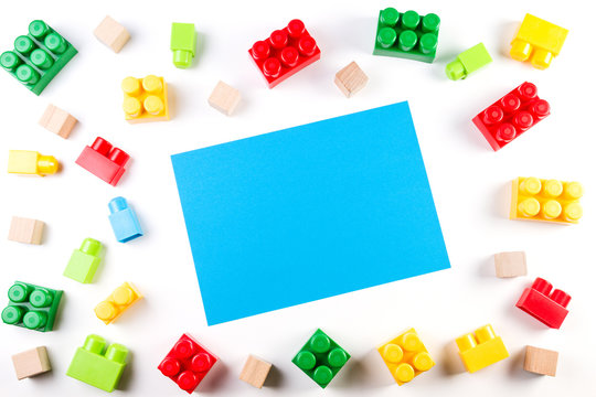 Colorful wooden cubes and plastic construction blocks with blue blank paper card on white background