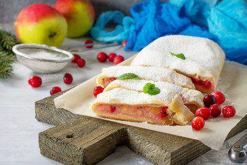Homemade apple strudel with fresh apples, cranberry and sugar powder on slate or stone background.