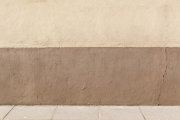 Aged street background. Beige and brown plastered wall and pavement.