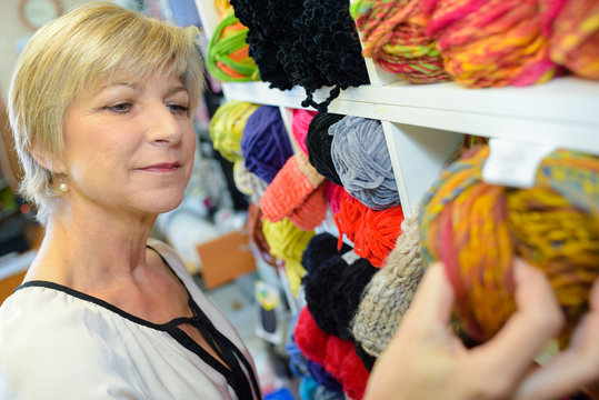 mature smiling blonde woman customer choosing multicolored spool with thread