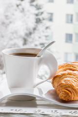 Hot Coffee cup with croissant on a frosty winter day window background