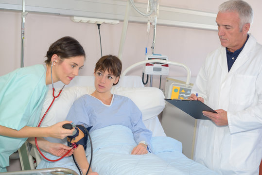 nurse taking blood pressure of female patient in hospital bed
