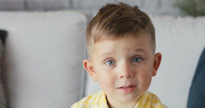 The boy serious looks at the camera sit on the sofa home moder design childhood close-up kid chid little emotions family Shot on RED EPIC camera. Slow Motion Shot.