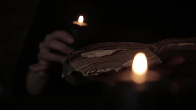 mystical beautiful witch in a black dress, casts a spell from old book with black candlelight