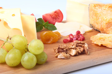 Assortment of cheese with fruits, grapes, nuts and cheese knife on a wooden serving tray.