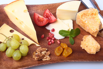 Assortment of cheese with fruits, grapes, nuts and cheese knife on a wooden serving tray.