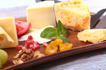 Assortment of cheese with fruits, grapes, nuts and cheese knife on a wooden serving tray.